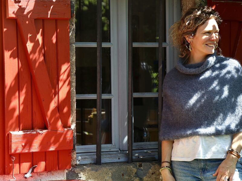 femme portant un chauffe épaules gris en extérieur ensoleillé devant fenêtre